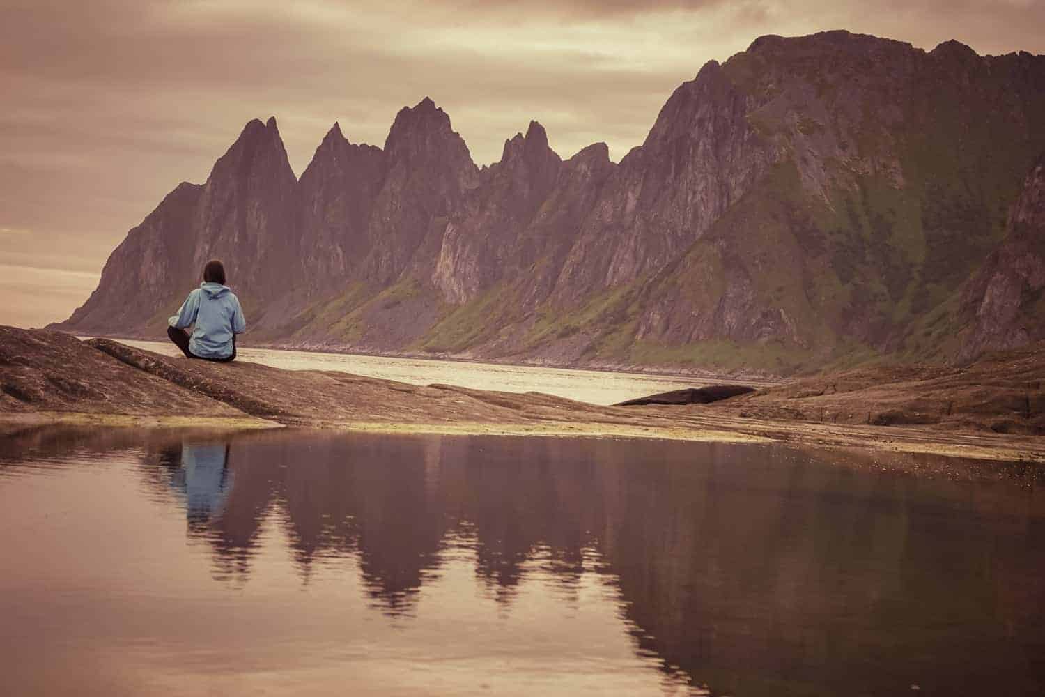 woman sitting on rocks in Senja island when traveling Norway by campervan
